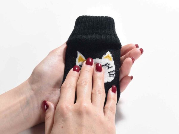 Scaldamani con copertura in maglia decorata con un musetto di gatto, fotografato in mano